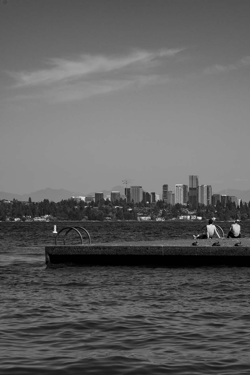 Two men resting on floating platform on Lake Washington looking out at Bellvue, Washington